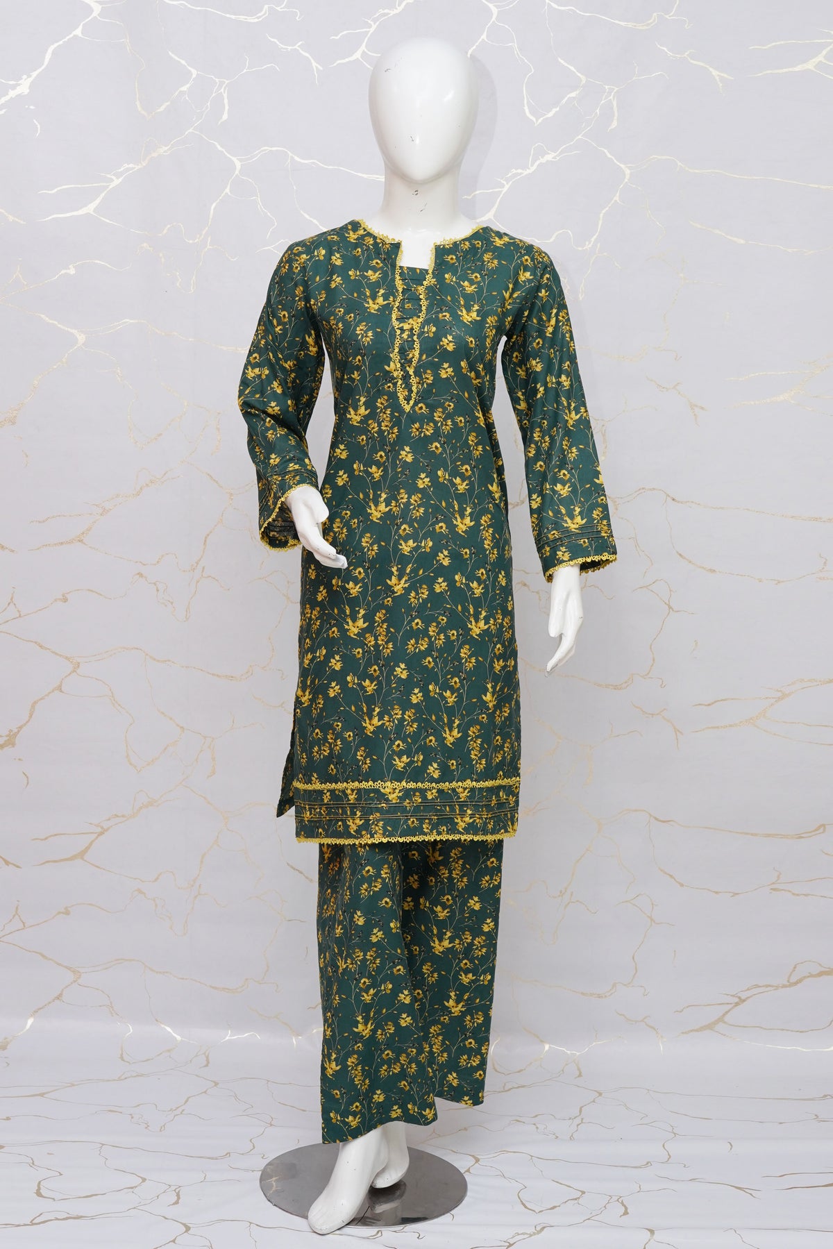 A dark green three-piece kurta set with a yellow floral pattern, displayed on a white mannequin against a light marble-patterned wall.